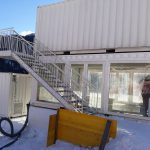 Container per eventi in ambiente invernale – Struttura a due livelli con scala esterna, realizzata con container bianchi, situata in un’area innevata.