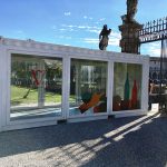 Container espositivo in location storica – Struttura bianca con vetrate personalizzate, posizionata in un’area monumentale per un evento di degustazione.