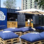 Container bar del Birrificio Angelo Poretti con area lounge esterna, arredato con pallet, cuscini e ombrelloni per il relax dei clienti.