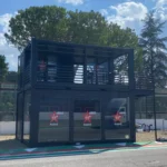 Struttura containerizzata Virgin Radio a due piani con pareti vetrate e terrazza superiore, installata presso autodromo per eventi live e trasmissioni radiofoniche.