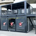 Struttura modulare a due piani brandizzata Virgin Radio, con ampie vetrate al piano terra, scala laterale in acciaio e terrazza panoramica superiore, installata all’esterno dello stadio.