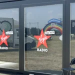 Dettaglio delle ampie vetrate della struttura Virgin Radio con loghi rossi Style Rock, riflessi del palco e arco scenografico visibili all’esterno durante un grande evento musicale.
