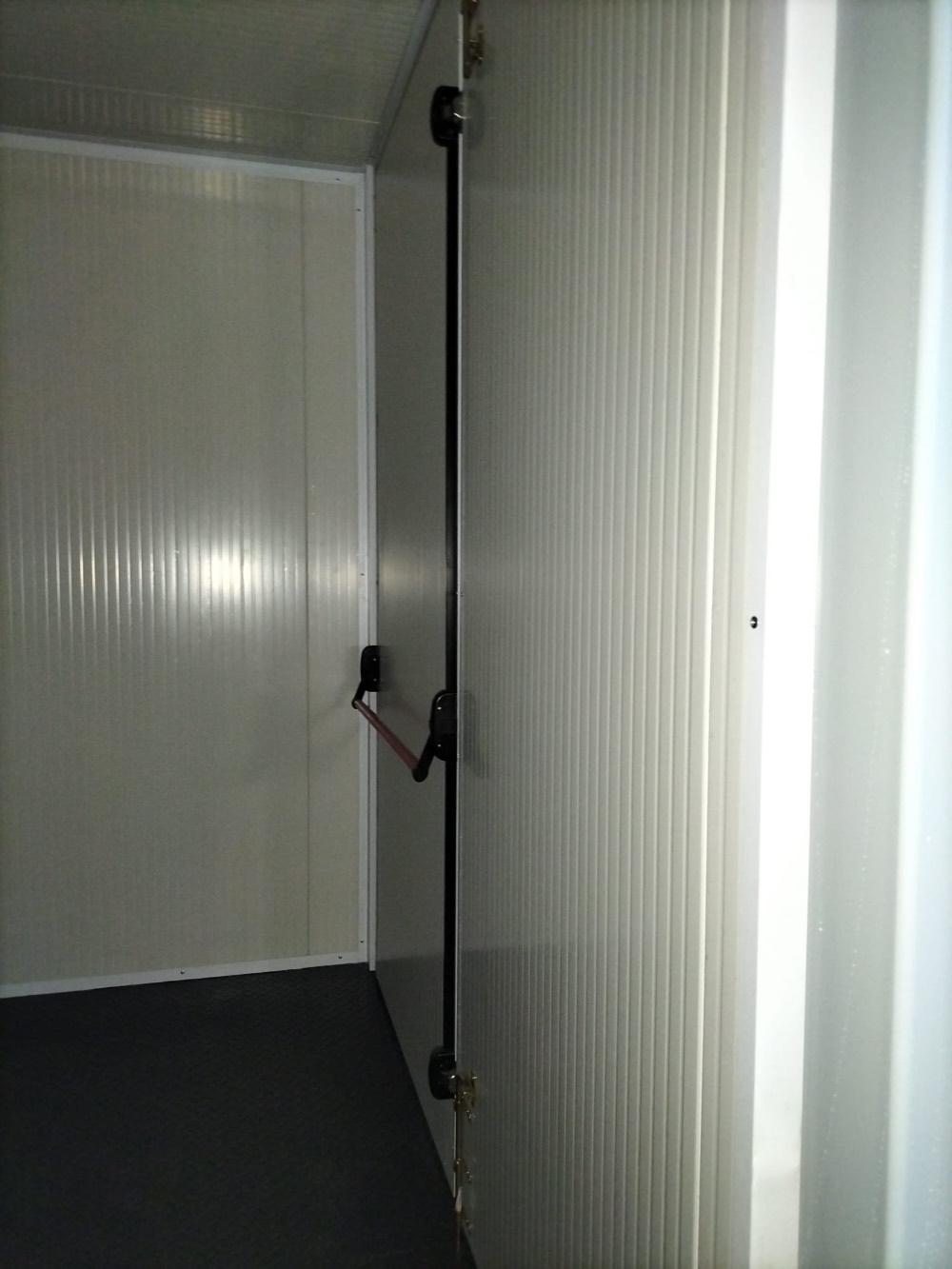 Interno di un container coibentato con porta dotata di barra antipanico, ideale per stoccaggio o ambienti a temperatura controllata.