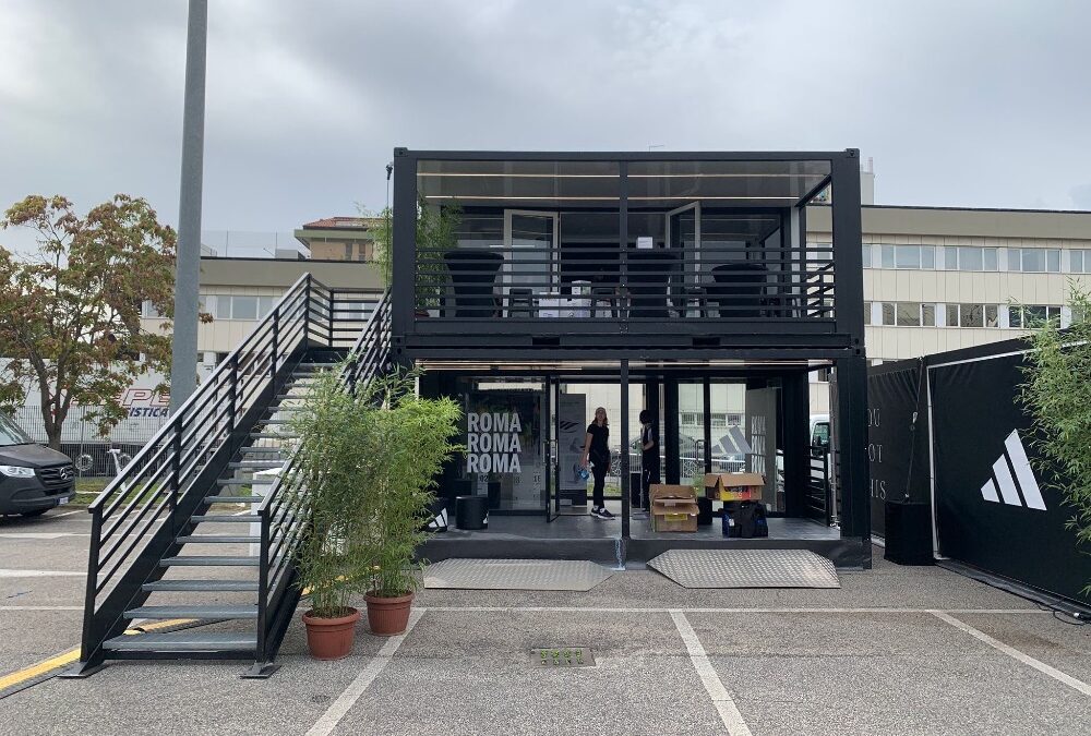 Container espositivo Adidas a due piani per la Mezza Maratona di Roma 2024, con struttura modulare nera, scale laterali e aree di accoglienza brandizzate.