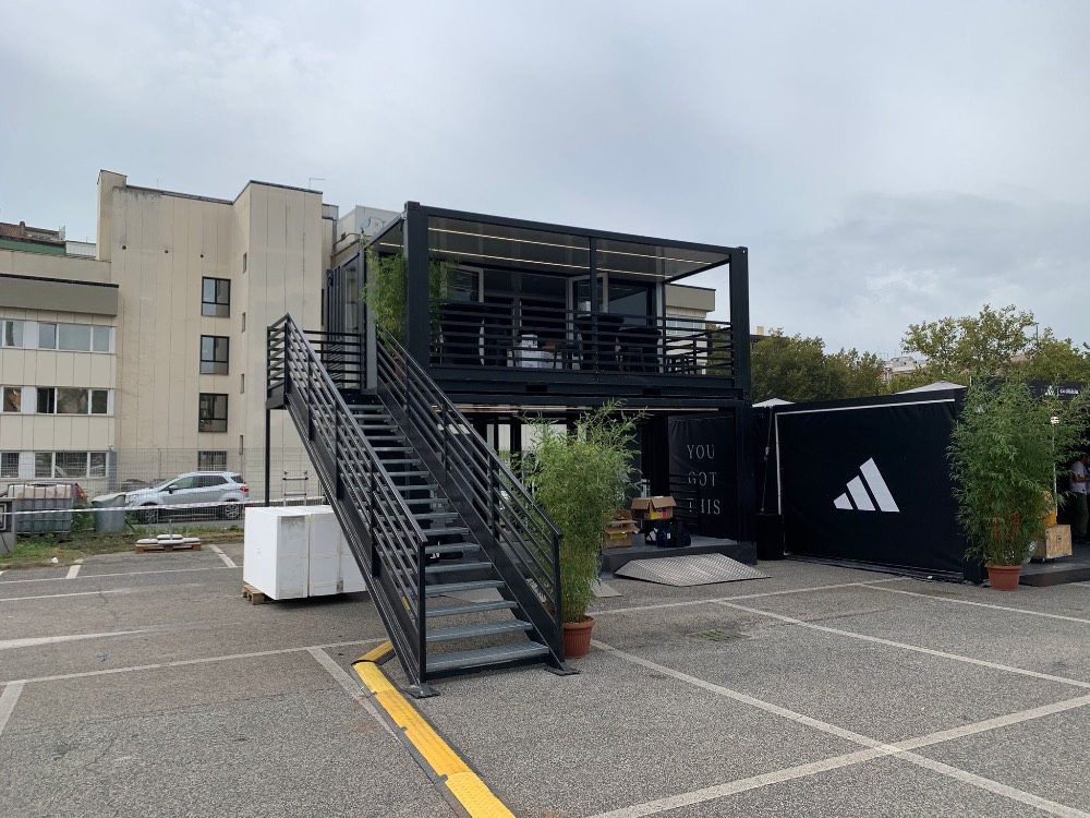 Vista laterale del container showroom Adidas, con terrazza panoramica superiore e ingresso al piano terra per l'esperienza evento durante la Mezza Maratona di Roma 2024.