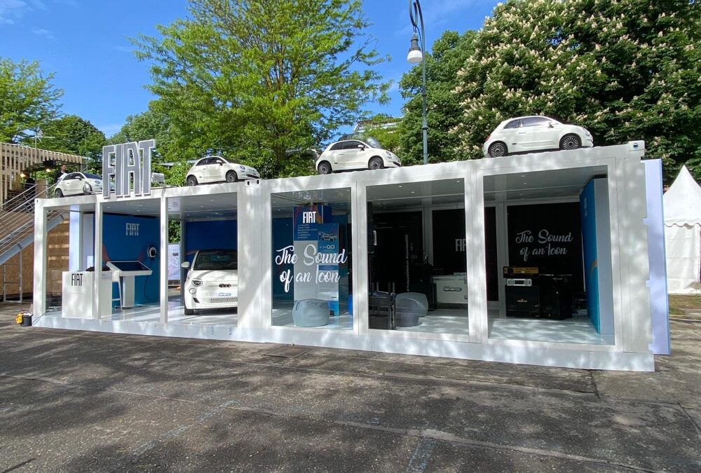 Vista d'insieme del container espositivo FIAT a Eurovision 2022, con auto esposte sul tetto e ampie vetrate per un ambiente aperto e accogliente.