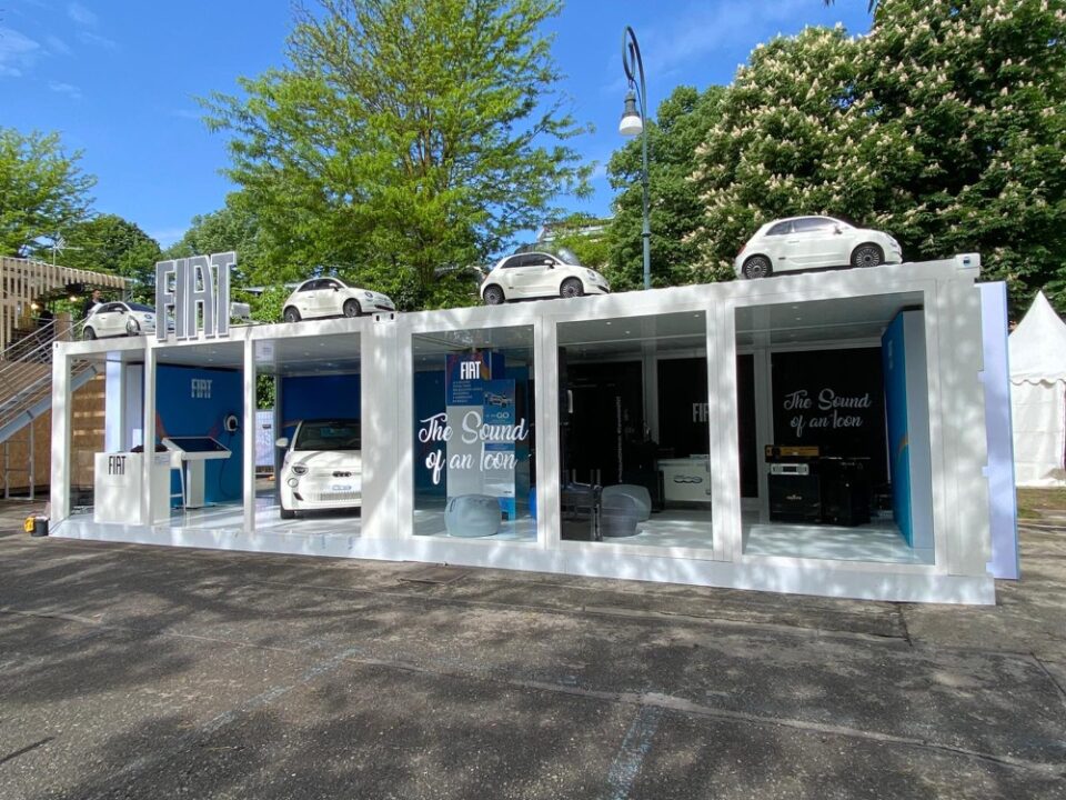 Vista d'insieme del container espositivo FIAT a Eurovision 2022, con auto esposte sul tetto e ampie vetrate per un ambiente aperto e accogliente.