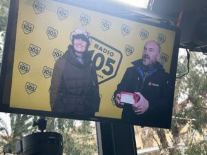 Schermo che mostra due persone in un’area dedicata a Radio 105 durante Sanremo 2025, con sfondo giallo brandizzato.