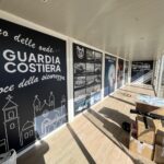 Interno dello showbox della Guardia Costiera con pannelli informativi e pavimentazione effetto legno