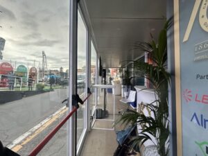 Interno del showbox vetrato dedicato ai 160 anni della Guardia Costiera a Sanremo, con arredi moderni, piante e area lounge per gli ospiti.