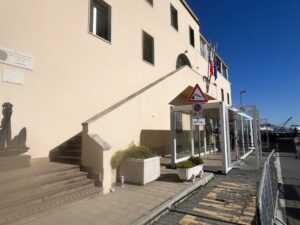 Struttura vetrata del container showbox vicino all’ingresso della Capitaneria di Porto, con segnaletica e accesso dedicato.
