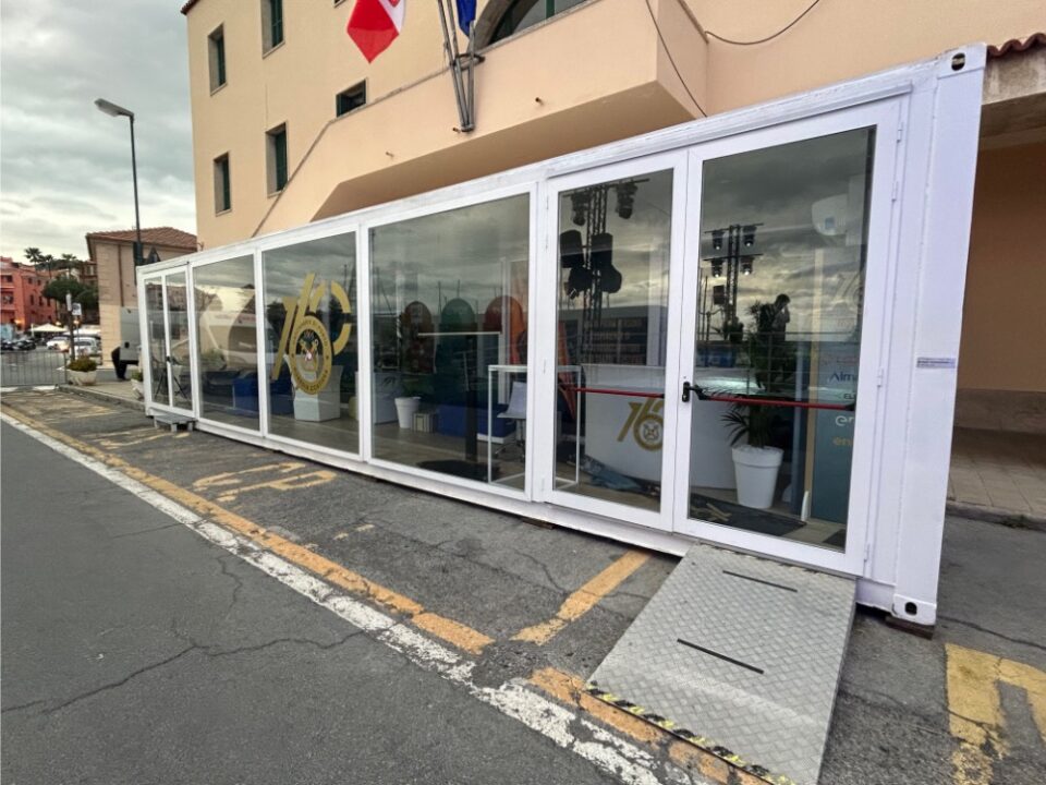 Vista laterale del showbox container per la Guardia Costiera, con ingresso principale, loghi ufficiali e installazione in una location strategica a Sanremo.