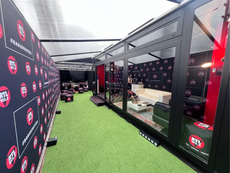 Area esterna dello studio RTL 102.5 a Sanremo 2025 con pareti brandizzate, prato sintetico e spazio lounge per ospiti e interviste.