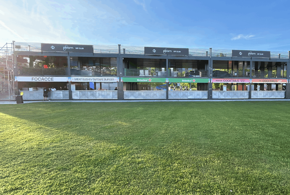 Struttura modulare a due piani realizzata con container Phoenix International per il Nameless Festival 2025, con aree food & beverage e terrazze VIP, allestita su prato verde.