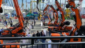 Vista dall’alto dell’area esterna dello stand Jekko a Bauma 2025, con diverse gru compatte arancioni in esposizione e visitatori in movimento.