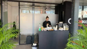 Operatrice al banco caffetteria dello stand Jekko a Bauma 2025, con snack, bevande e attrezzature per l’ospitalità, allestito all’interno della struttura modulare.