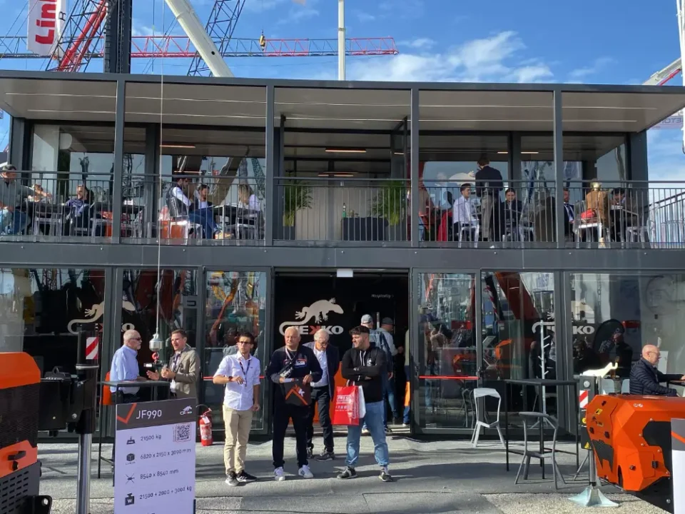 Struttura espositiva modulare a due piani realizzata da Phoenix International per Jekko a Bauma 2025, con terrazza panoramica e aree meeting, visitatori all'ingresso e ospiti nei saloni superiori.