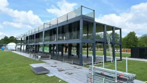 Struttura containerizzata su due livelli in fase di assemblaggio, realizzata da Phoenix International per il Nameless Festival 2025, su prato verde e con moduli prefabbricati in acciaio.