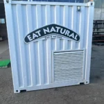 Retro del container promozionale Eat Natural di Ferrero, con logo frontale in evidenza e pannelli in acciaio bianco. Struttura compatta, resistente e facilmente trasportabile, ideale per tour e roadshow brandizzati.