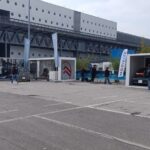 Diversi container espositivi allestiti per i brand dell’area Your Urban Mobility a EICMA 2025, con veicoli elettrici in mostra e visitatori che esplorano gli spazi esterni del polo fieristico.