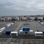 Vista aerea dell’allestimento dell’area Y.U.M. a EICMA 2025, con numerosi container bianchi e blu disposti nell’ampio piazzale esterno durante la fase di preparazione.