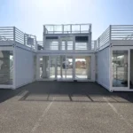 Struttura container modulare su più livelli con area centrale vetrata per accoglienza e meeting