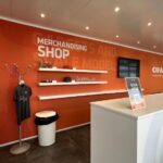 Spazio merchandising CIFA con bancone personalizzato, espositori a parete, monitor e grafiche arancioni.