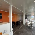 Ambiente interno CIFA con area lounge, tavoli per l’accoglienza e vetrate a tutta altezza.