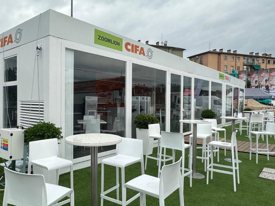 Struttura modulare vetrata CIFA e Zoomlion a SaMoTer, con area hospitality esterna arredata con tavoli e sedute.