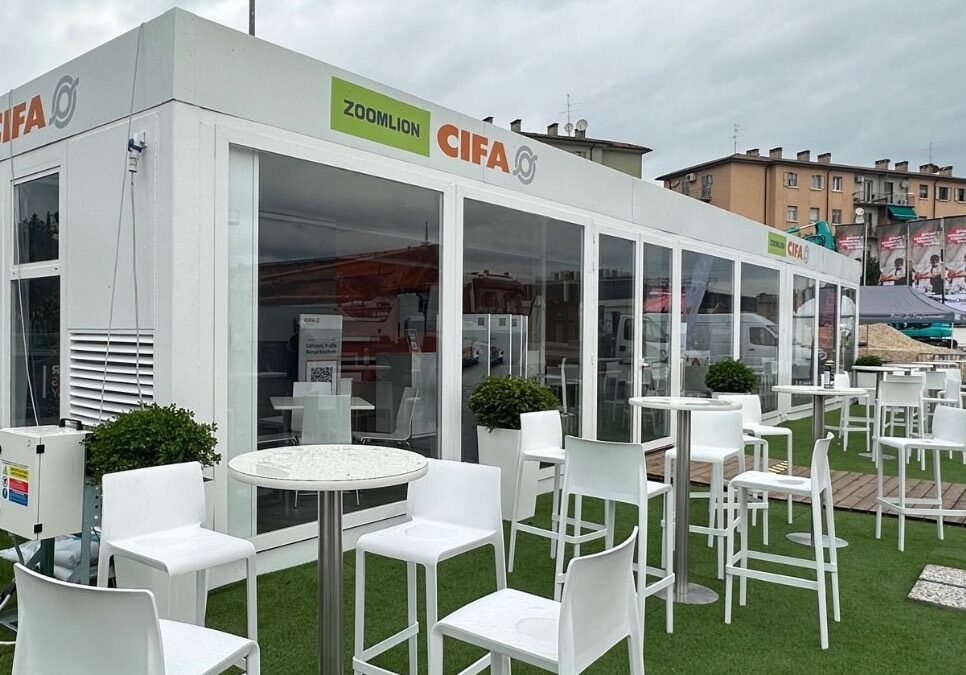 Struttura modulare vetrata CIFA e Zoomlion a SaMoTer, con area hospitality esterna arredata con tavoli e sedute.