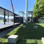 Dettaglio laterale della struttura modulare con container, pilastri di sostegno e basamenti in calcestruzzo.